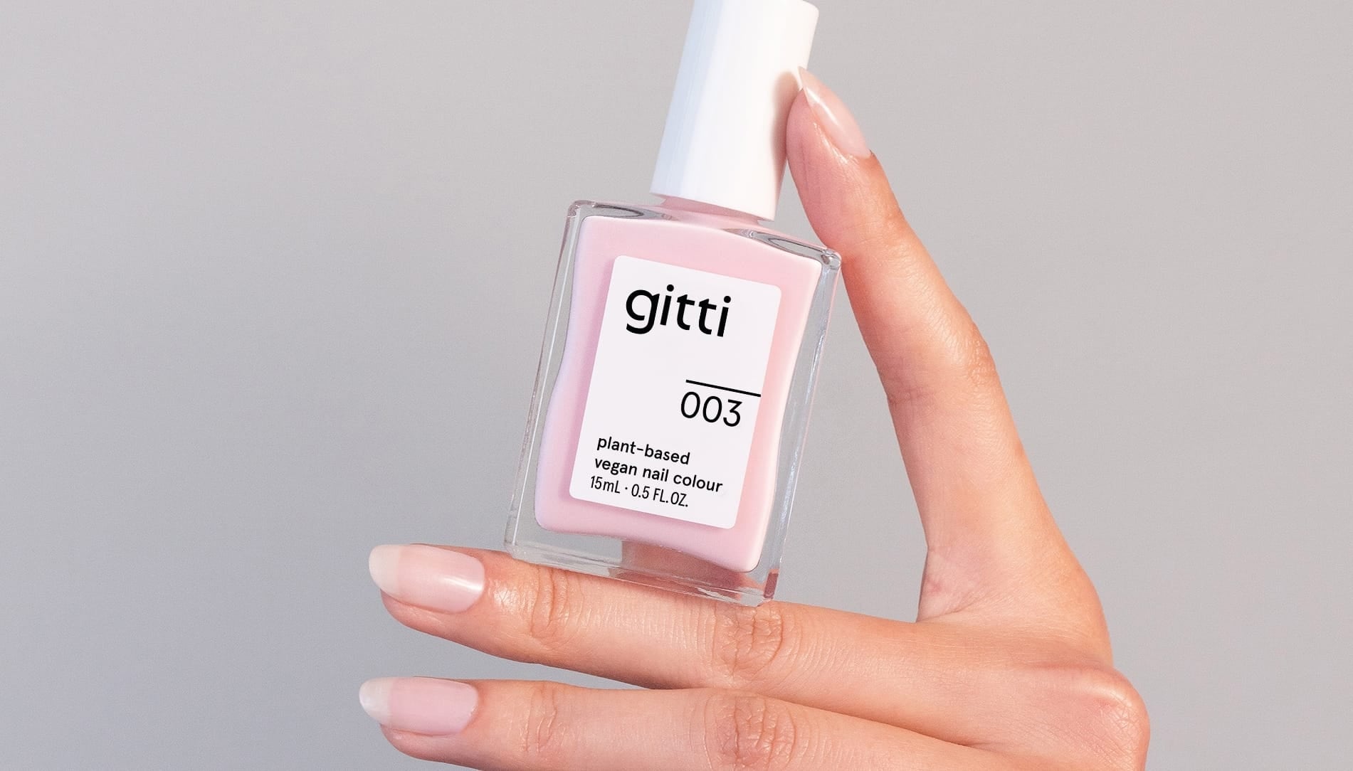 Bottle of gitti nail polish no. 003 sheer pink held by a hand against a gray background