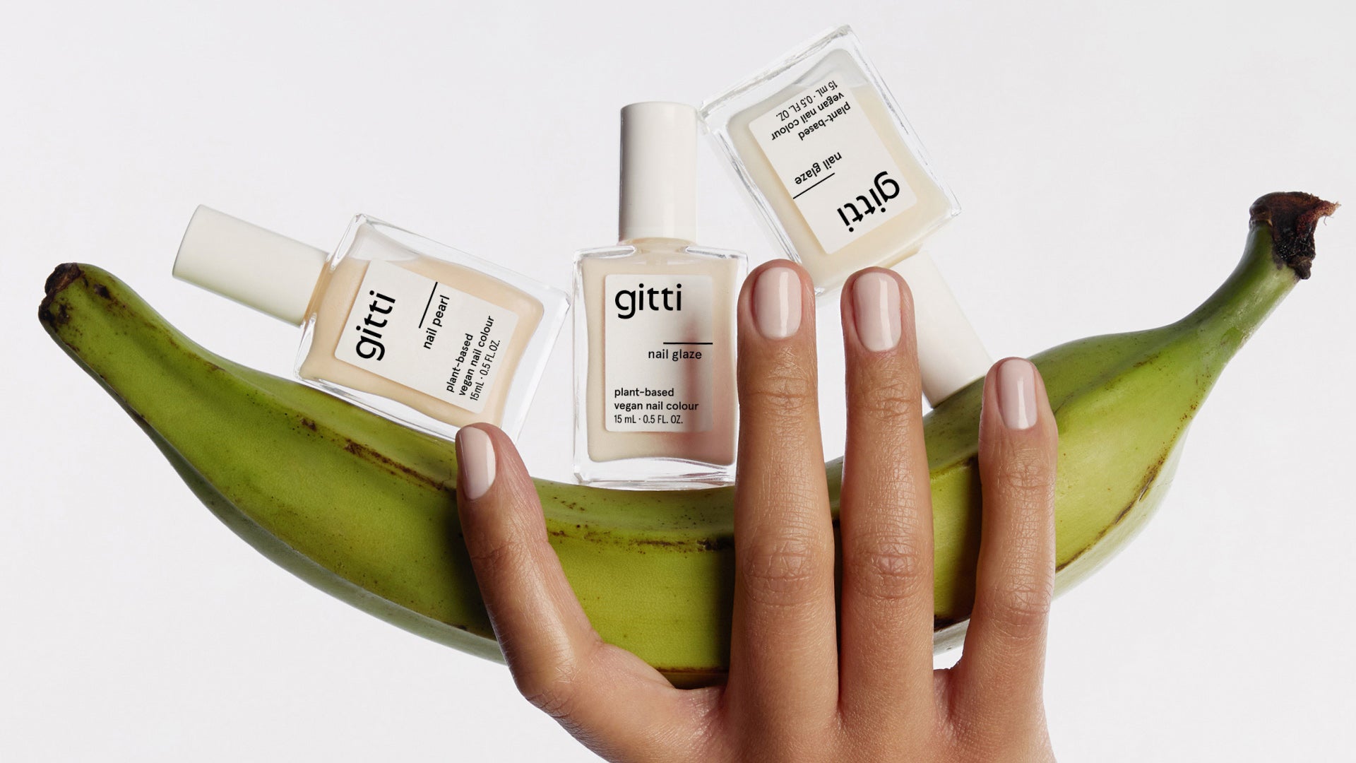 three gitti nail polish bottles on a banana held by a hand with a glaze manicure