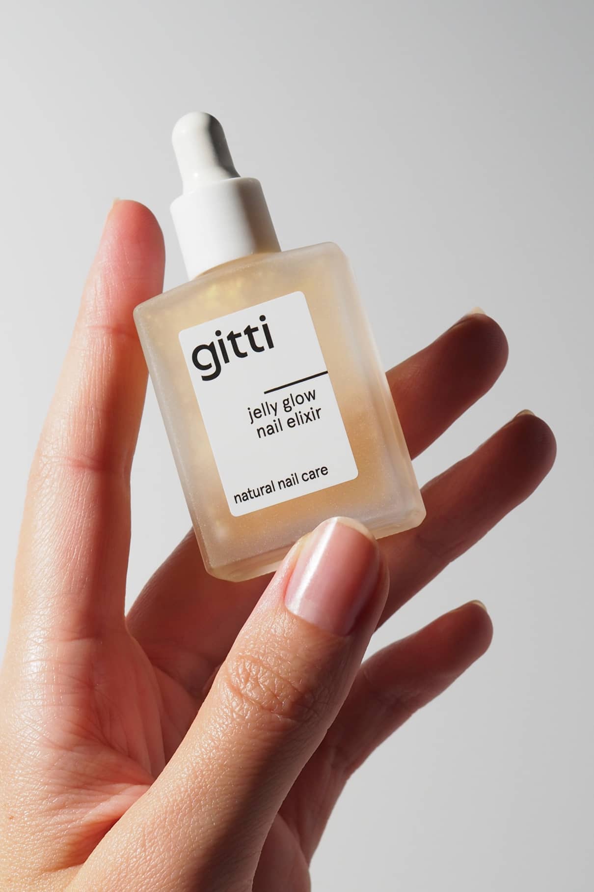 Hand holding a bottle of gitti jelly glow nail elixir against a neutral background