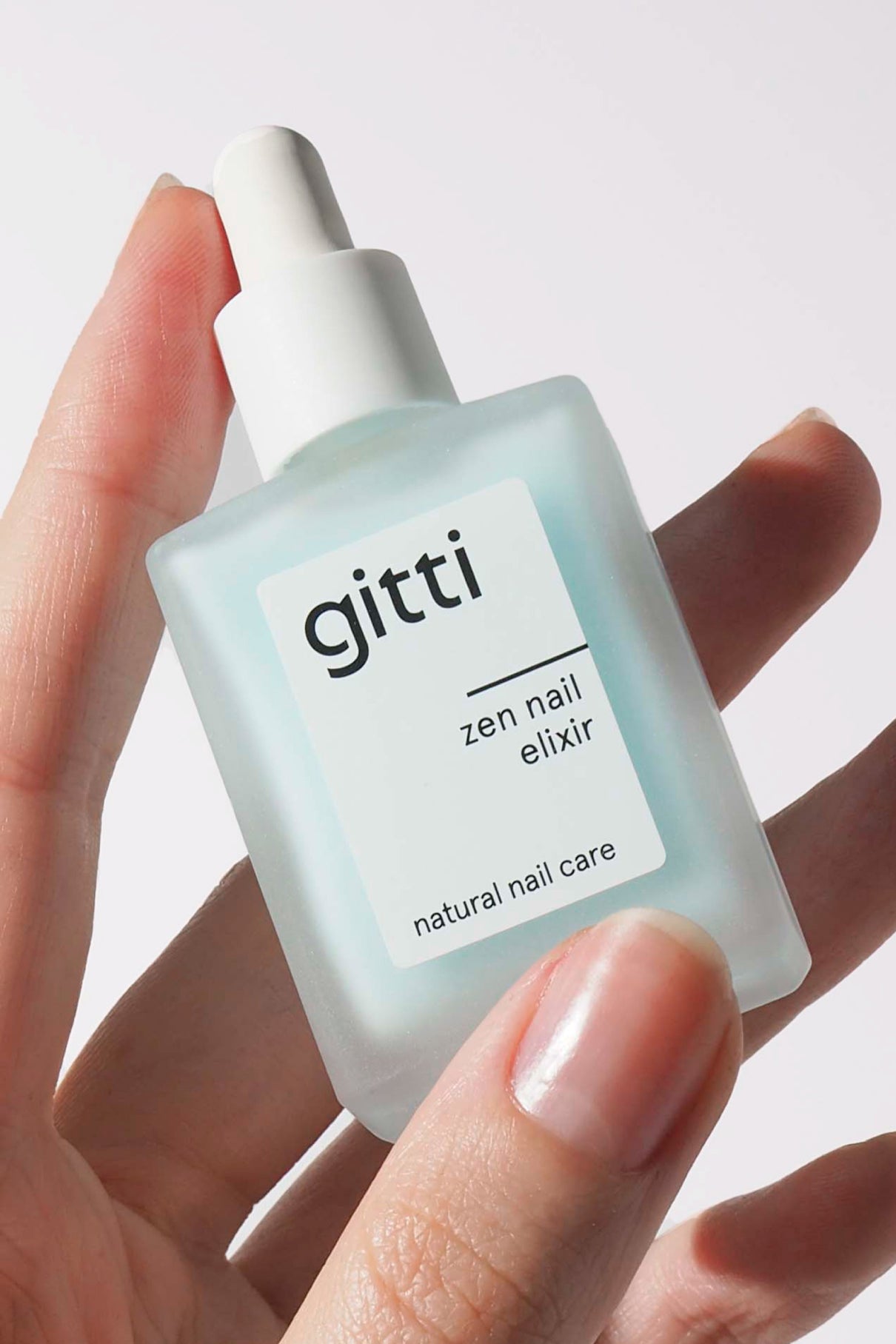 Gitti zen nail elixir bottle held in a hand with a light background
