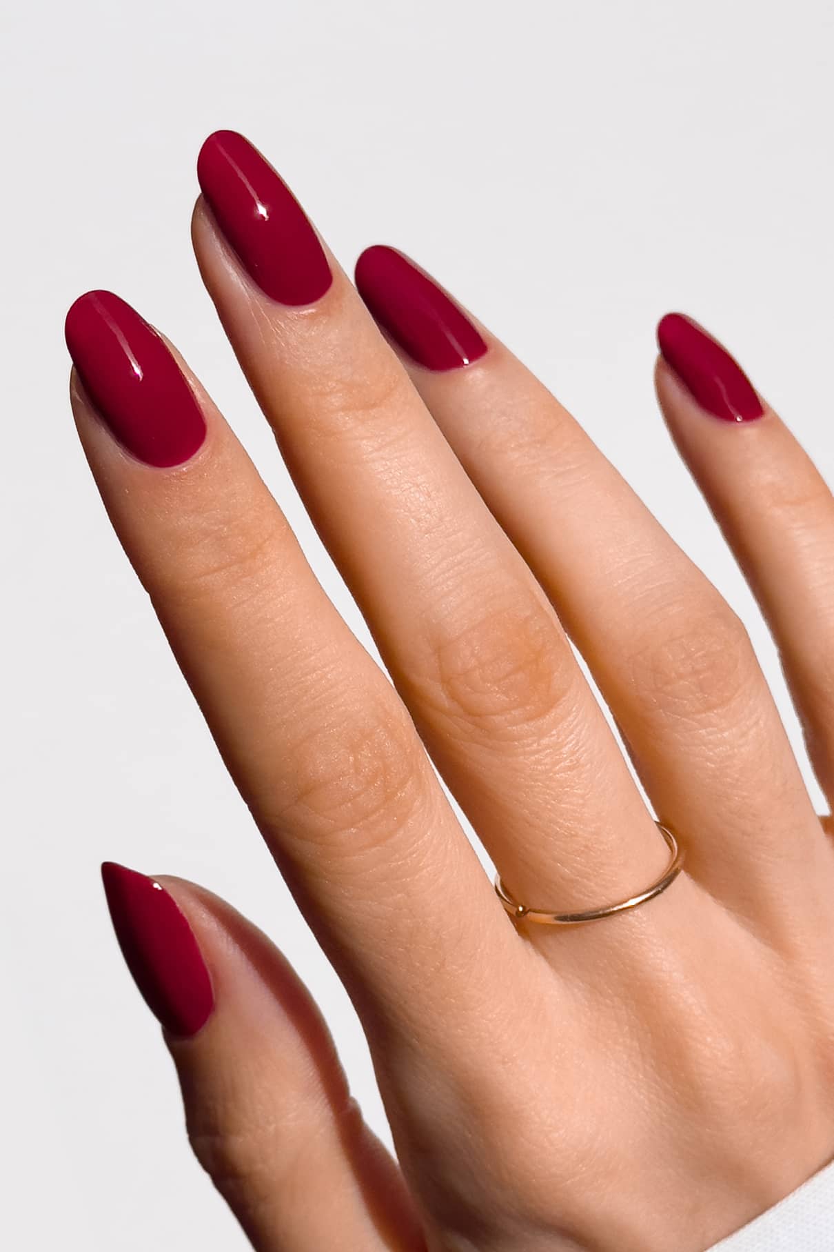 Hand with red nail polish and a gold ring on a light gray background