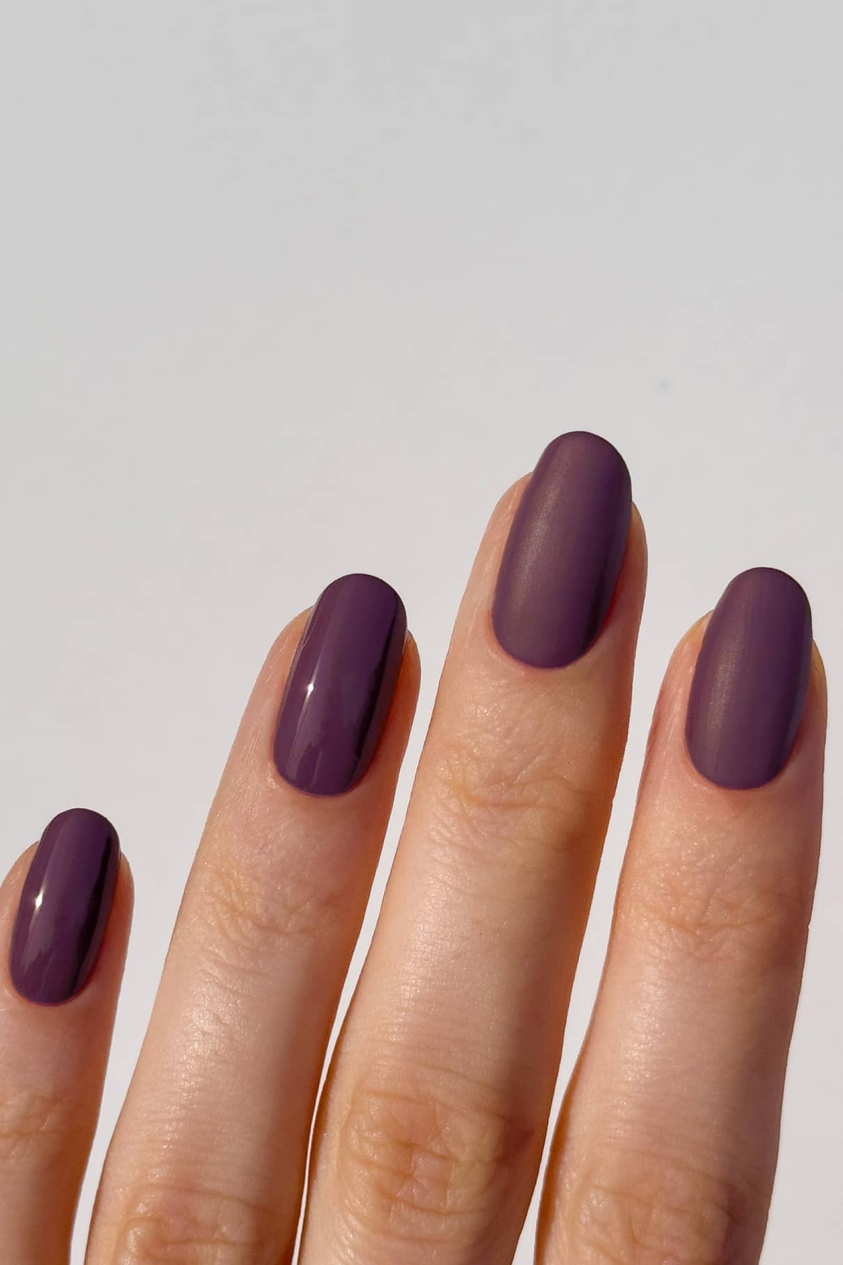 Hand with purple nail polish on a light gray background