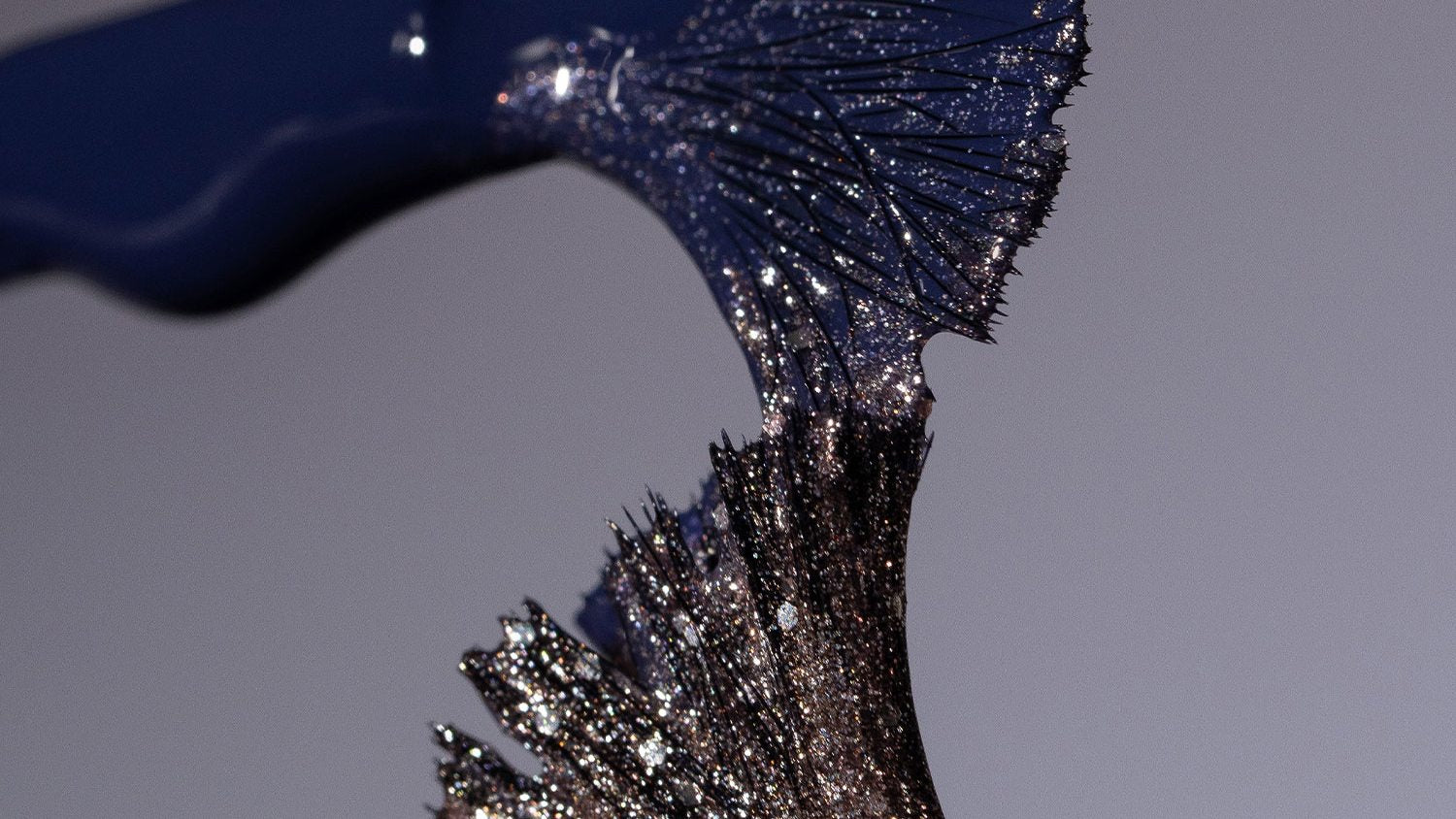 Close-up of a dark blue and black textured nail polish brush against a gray background