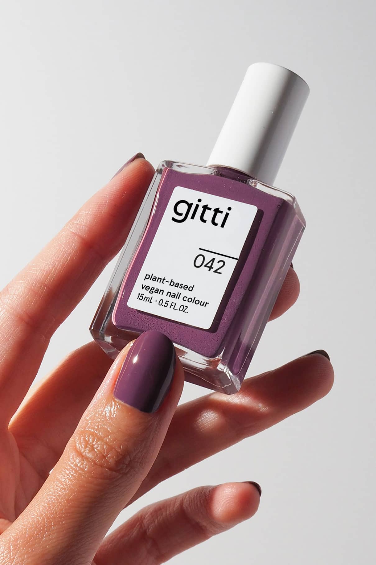gitti nail polish bottle with a hand wearing a matching purple nail color on a neutral background